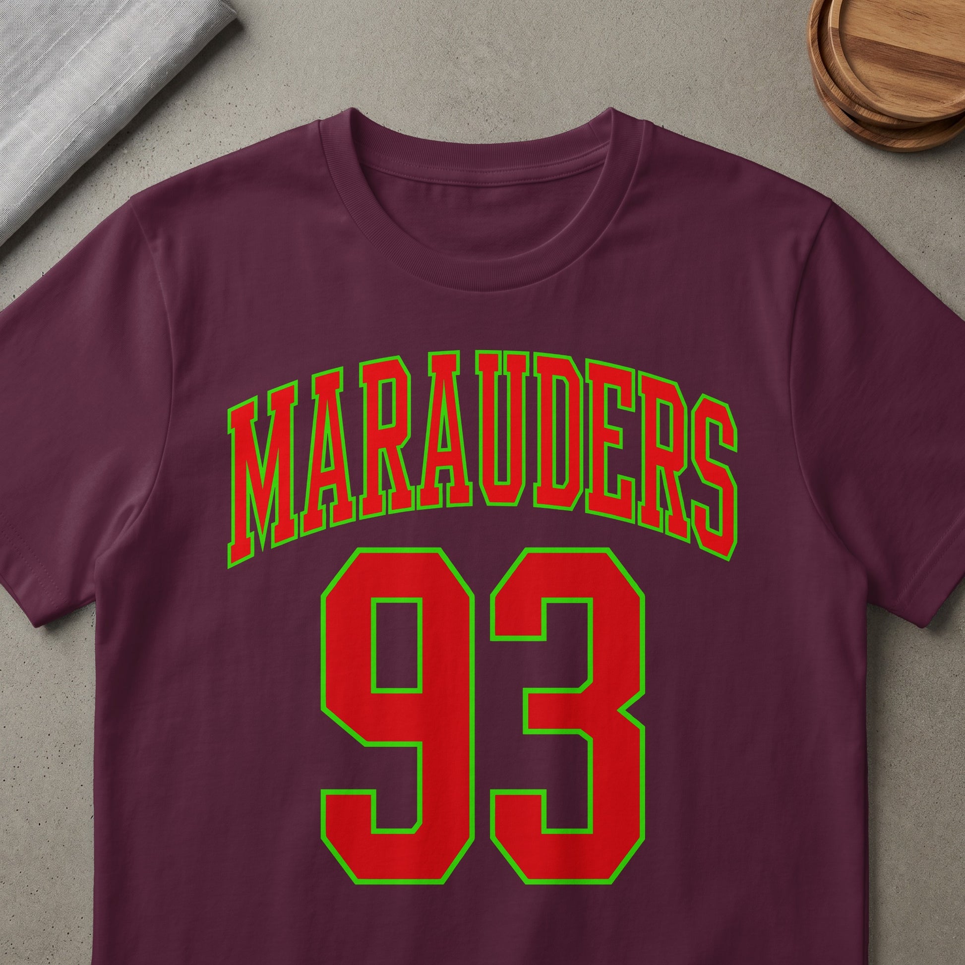 Maruaders 93 text in red with green outline on a maroon t-shirt.